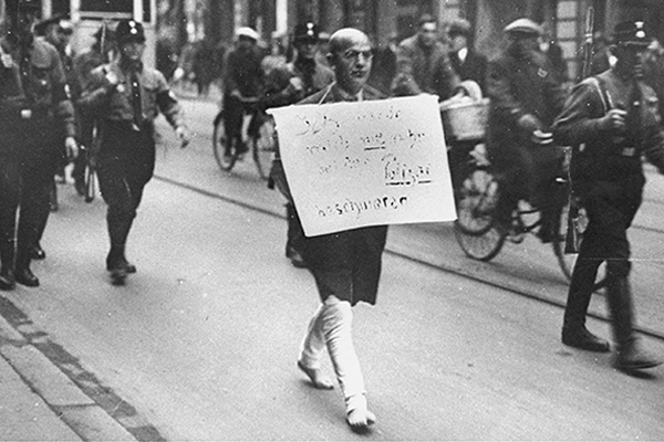 In March 1933, Dr. Michael Siegel, a respected Jewish attorney from Munich, is forced to walk barefoot through the streets wearing a sign that reads, "I am a Jew, but I will never again complain to the police." Bundesarchiv Bild 146-1971--006-01