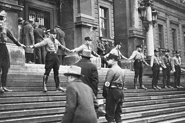A group of SA hold hands on the steps of the University of Vienna in an attempt to prevent Jews from entering the building. The action led to a day of student rioting, which had to be suppressed by police, circa 1938. National Archives