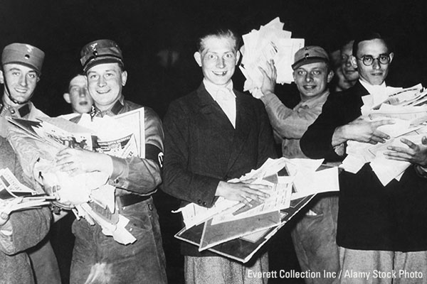 Nazi Storm troopers and young German men holding pictures and pamphlets at a public book burning. Ca. 1933-1940. Everett Collection Inc / Alamy Stock Photo